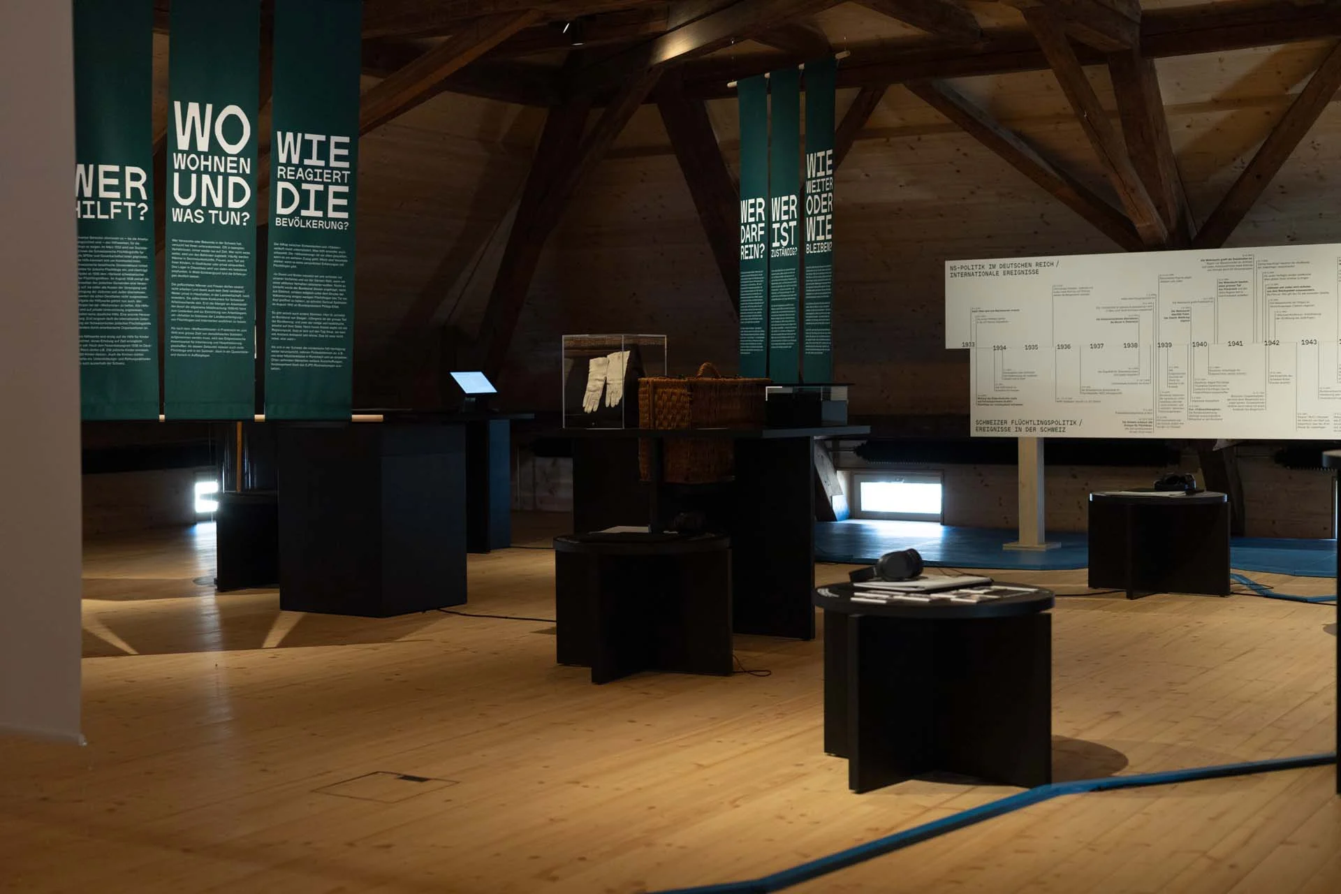 Moderne Museumsausstellung mit grünen Bannern, Schweizer Denkmal und schwarzen Ausstellungstischen.